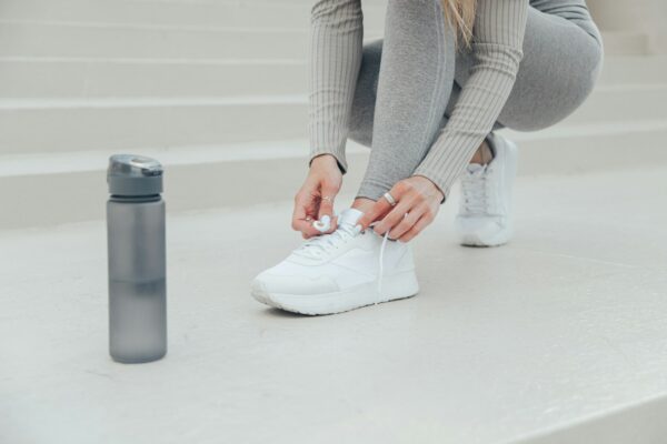 Young woman tying white sports shoe. Grey sport bottle with water