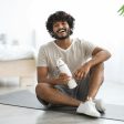 Positive indian guy drinking water while having workout